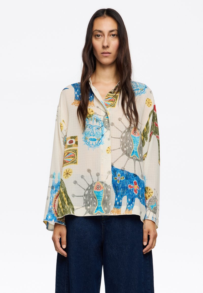 Camicia a maniche lunghe, con bottoni, in tessuto color crema chiaro, caratterizzata da motivi di animali e geometrici colorati in blu, verde, rosso e giallo.