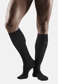 Calcetines negros hasta la rodilla hechos de material elástico, con parte superior acanalada y textura suave, posicionados sobre un par de piernas.