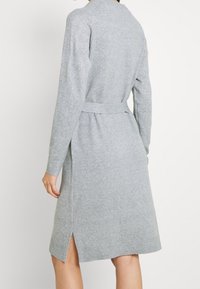 Cardigan grigio a maglia con maniche lunghe, vita cinturata e spacchi laterali. Tessuto morbido e texturizzato con polsini e orlo a costine.