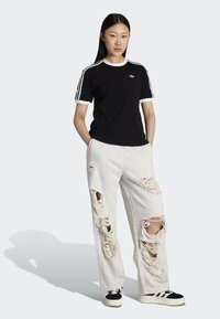 Black t-shirt with white accents and three stripes on sleeves, paired with grey sweatpants featuring large distressed rips and white detailing.