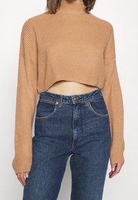 Béžový krátký pletený svetr s vysokým límcem a volnými rukávy, kombinovaný s modrými džínami s vysokým pasem a pěti kapsami.