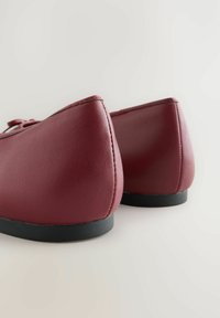 Burgundi nahkakengät pyöristettyjä takapintoja, mustat kumipohjat ja sileä pinta. Vähäiset ompeluyksityiskohdat reunoilla.