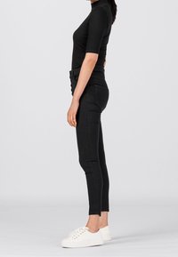Top negro de cuello alto acanalado combinado con jeans ajustados negros de tiro alto y zapatillas blancas, mostrando una silueta esbelta y un diseño simple.