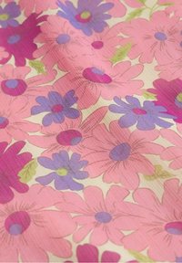 Tissu à motifs avec de grandes fleurs roses, violettes et magenta ainsi que de petites feuilles vertes sur un fond crème clair.