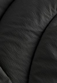 Gros plan sur du cuir noir montrant une surface douce et texturée avec de fines rides. Présente des coutures lisses le long des bords.