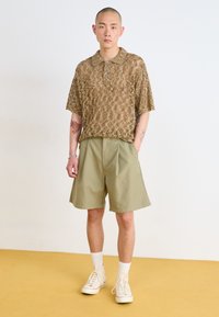 Brown, short-sleeved mesh polo shirt with a collar and button, paired with light green knee-length shorts. White high-top sneakers and socks.