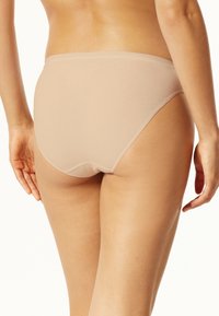 Béžové vysoké spodní prádlo vyrobené z hladkého, pružného materiálu. Vyznačuje se minimalistickým designem s bezešvým provedením a bez viditelného příslušenství.