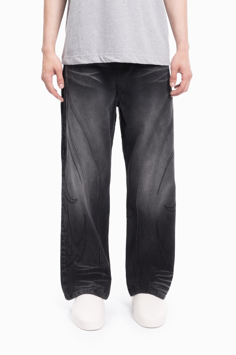 Jeans negri din denim cu picioare largi, având cusături cu model ton pe ton de-a lungul cusăturilor și o textură ușor decolorată. Modelul poartă încălțăminte minimalistă.
