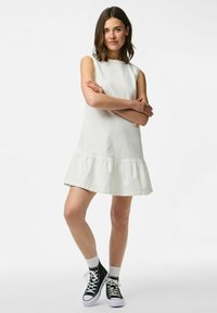 Balta, bez piedurknēm, kleita ar izplūdušu, viļņotu apakšdaļu. Audums šķiet mīksts ar gludu faktūru. Valkāta kopā ar melniem un baltiem sporta apaviem.