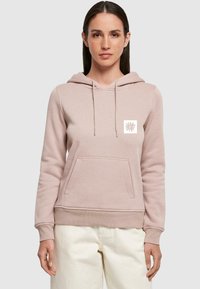 Ljusrosa hoodie med kängurufickor, dragsko på huven och en blommig logotyp på bröstet. Mjukt material med ribbad mudd och nederkant.