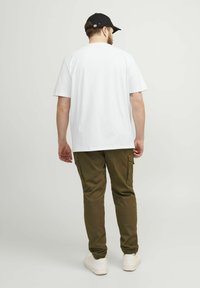 Vit bomull T-shirt med avslappnad passform, parat med olivgröna cargobyxor med sidofickor och vita sneakers. En svart keps fulländar looken.