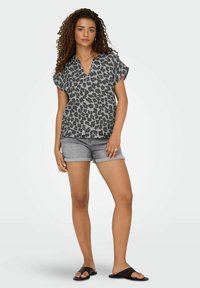 Grå leopardmønstret bluse med korte ærmer og V-hals, parret med grå denimshorts. Emnet står barfodet i sorte slidesandaler.