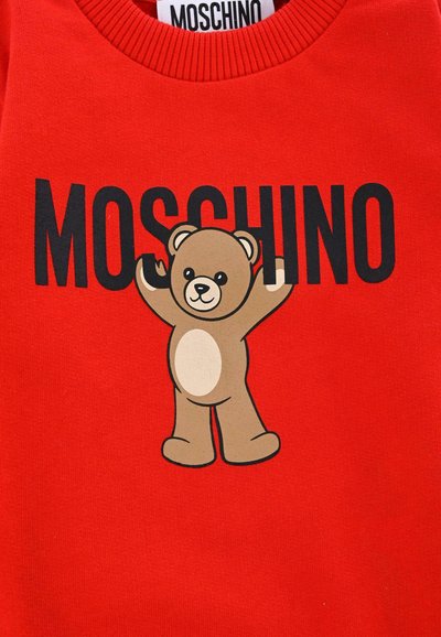 Felpa rossa con un design di un orso cartone animato in beige e testo nero con scritto "MOSCHINO". Il tessuto ha una superficie liscia con colletto a coste.