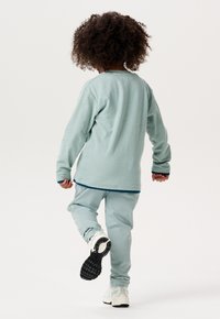 Mintgrünes Langarmshirt mit geripptem Muster, kombiniert mit passenden Jogginghosen. Das Outfit hat elastische Bündchen und Sneakers mit schwarzer Sohle.
