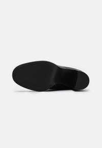 Suela de zapato negra con textura lisa, con forma redondeada, tacón ligeramente elevado y diseño minimalista. Sin patrones ni acentos visibles.