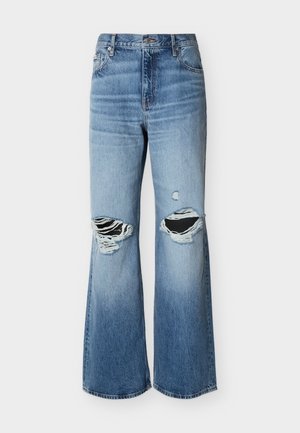 Jean en denim délavé bleu à jambes larges avec de grands trous déchirés aux deux genoux, sur fond blanc.