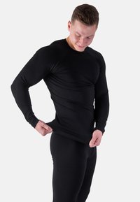 Schwarzes, langärmliges Sportoberteil aus dehnbarem Material, enganliegendes Design mit glatter Textur, kombiniert mit passenden schwarzen Leggings.