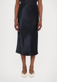 Satin svart midi kjol med en slät yta, något utfälld fåll och h�ög midja. Kombinerad med ljusa spetsiga skor.