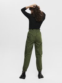 Pantalones cargo verdes con cintura elástica, tobillos ajustados y bolsillos laterales. Combinados con una blusa negra de manga larga y sandalias de tacón negras.
