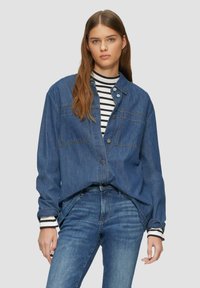 Jeanshemd, hellblau mit lockerer Passform, Knopfverschluss vorne, zwei Brusttaschen und langen Ärmeln, über einem gestreiften Oberteil getragen.