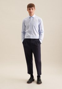 Camicia azzurro chiaro con taschino sul petto, abbinata a pantaloni scuri su misura e scarpe nere. Tessuto fresco, design slim fit.