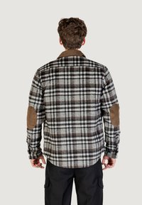 Camicia di flanella a scacchi in nero, bianco e marrone con toppe in velluto a coste marroni sui gomiti e un collo marrone a contrasto.