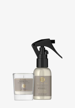 Een helder glazen kandelaar met een label; daarnaast staat een goud-zwart spuitflesje met het label "Royal Tea" voor huisparfum.