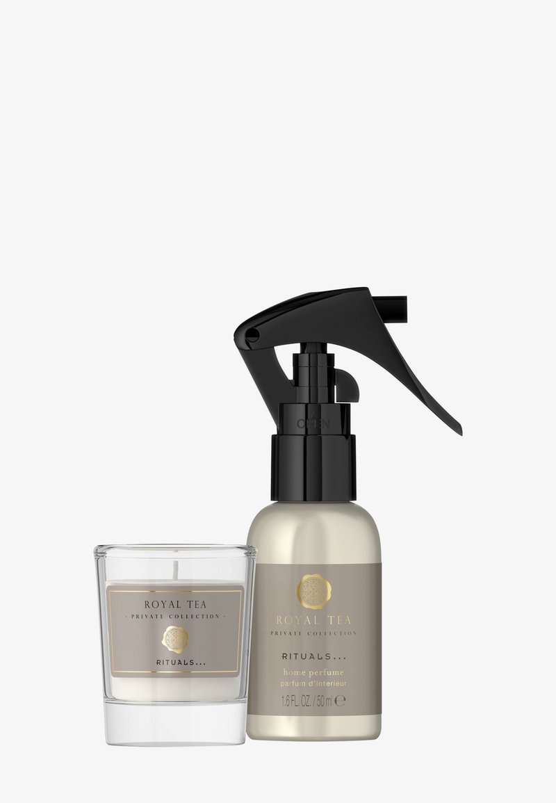 Een helder glazen kandelaar met een label; daarnaast staat een goud-zwart spuitflesje met het label "Royal Tea" voor huisparfum.