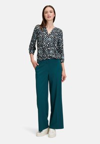 Blouse à motifs noir et canard avec un col en V, assortie à un pantalon large canard et des baskets blanches. Tissu lisse.