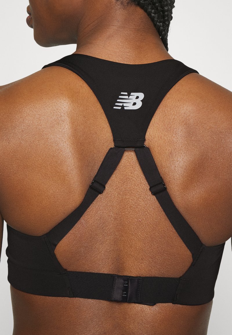 Sujetador deportivo negro con diseño de espalda nadadora, que cuenta con tirantes ajustables y un cierre con gancho. Logo impreso en la parte posterior. Textura de tela suave.
