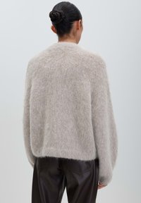 Woman with dark hair in a bun wearing a fuzzy beige sweater and black leather pants, shown from the back against a plain background.