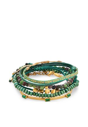 Stak af grønne og gyldne perle- og flettede armbånd med gyldne accenter og grønne ædelstene på en hvid baggrund.