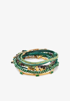 Stak af grønne og gyldne perle- og flettede armbånd med gyldne accenter og grønne ædelstene på en hvid baggrund.