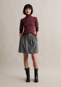 Burgundy long-sleeve turtleneck shirt paired with a gray knee-length skirt featuring pinstripes and an elastic waist. Black knee-high boots.