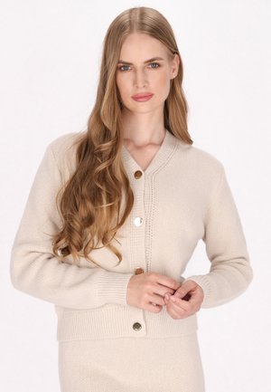 Cardigan lavorato a maglia beige con scollatura a V, maniche lunghe e polsini a coste. Presenta bottoni in tonalità oro e cuciture strutturate lungo la parte anteriore.