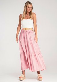 Rosa gestufter Maxirock mit einem Taillengürtel und einer runden Schnalle, aus leichtem Material, kombiniert mit einem weißen gerippten Oberteil und Plateausandalen.