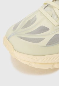 Sapatilhas com um parte superior amarelo pálido e painéis de malha cinza, recortes alongados em forma de folha e uma sola de borracha texturizada em creme.