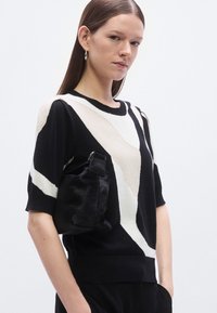 Čierno-biely sveter s geometrickými vzormi, krátkymi rukávmi, okrúhlym výstrihom a textúrovanou, mäkkou čiernou taškou s remienkom.