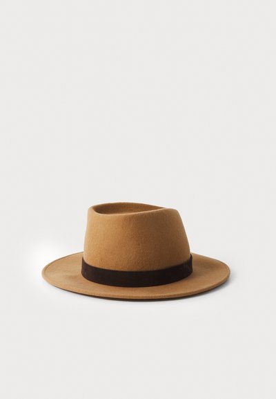 Chapeau fedora en feutre marron avec un large bord et un bandeau marron foncé. Il présente un sommet arrondi et une texture douce.