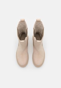 Beige Knöchelstiefel aus weichem Wildleder mit glatter Oberfläche, ausgestattet mit einer Ziehschlaufe und runder Zehenpartie. Innenausstattung aus plüschigem Material.