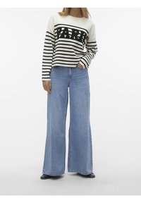 Pull rayé blanc et noir avec le texte "PARIS". Associé à un jean en denim bleu à jambes larges. Texture lisse, coupe décontractée et design casual.