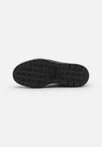 Suela de zapatilla de goma negra con patrón texturizado, que presenta un diseño de agarre hexagonal y una placa central con el logo.