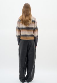 Strickpullover in Creme mit einfarbigen Streifen (braun, marineblau, orange) und geripptem Saum, kombiniert mit weiten schwarzen Lederhosen.