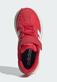 Červená športová obuv s vrchom zo semišu a sieťoviny, bielymi akcentmi, šnúrkami a suchým zipsom; má polstrované golier a čiernu stielku.