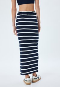 Marineblauw en witte gestreepte maxi rok met een elastische tailleband, gemaakt van zachte stof, in combinatie met casual witte schoenen.