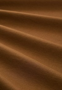 Bruine stof met een gladde textuur, voorzien van zachte plooien en een subtiele glans. Het oppervlak vertoont een geborstelde uitstraling met fijne lijnen.