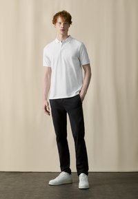Witte polo met korte mouwen, gecombineerd met donkere slim-fit broeken en witte sneakers. Glad katoen textuur en eenvoudig ontwerp.