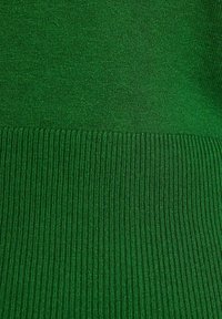 Maglione verde a maglia con la parte superiore liscia e testurizzata che si trasforma in un orlo a coste nella parte inferiore. Colore uniforme su tutta la superficie.