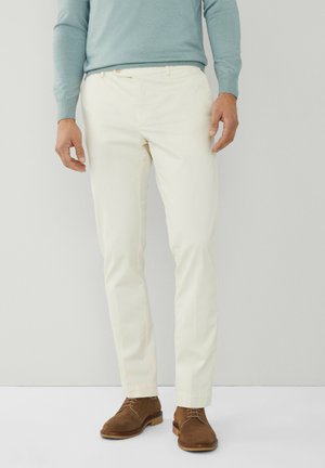 Pantalones de corte ajustado color crema con bolsillos frontales, diseño de frente plano y ajuste entallado, combinados con zapatos de ante marrón.