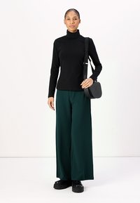 Zwarte lange mouw turtleneck top gecombineerd met wijde, donkergroene broek. Gecombineerd met een kleine zwarte crossbody tas en zwarte platform schoenen.
